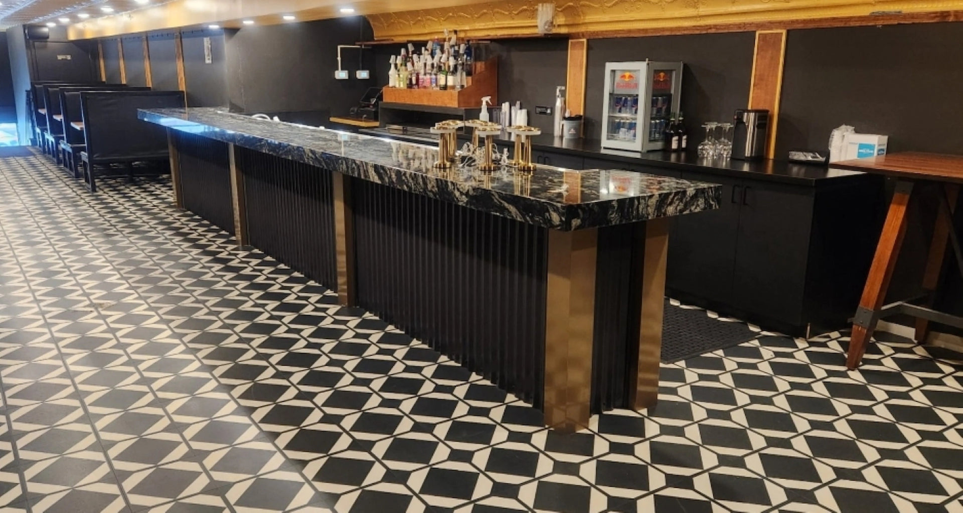 Modern bar with black granite countertop, gold accents and black and white tiled floor
