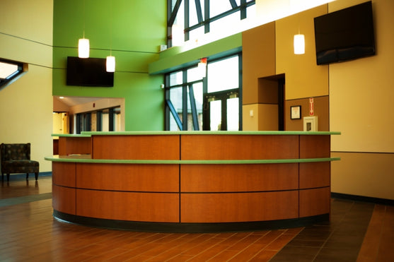 Modern interior with a curved laminate reception desk with solid surface countertops against a green wall.