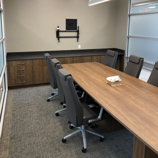 Modern conference room with a long wooden table and gray chairs.