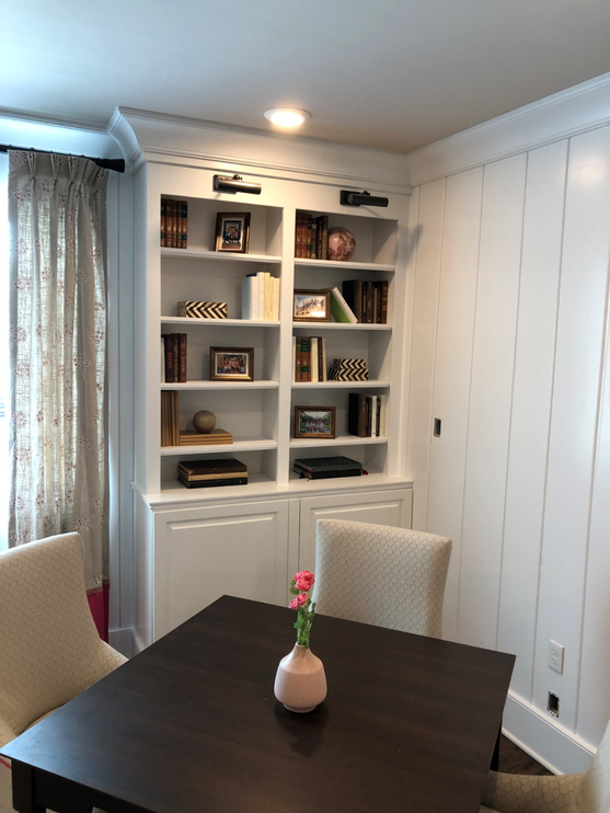 Room with a dark wooden table and chairs, and a white bookshelf filled with books and decorative items.