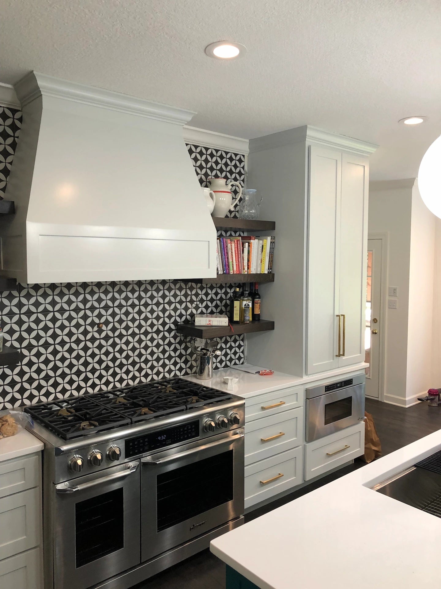 Modern kitchen with custom painted cabinets, custom wood exhaust hood cover, stained wooden floating shelves, stainless steel appliances, quartz countertops and geometric tile backsplash