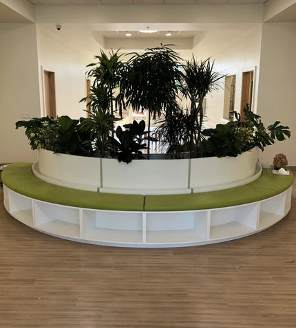 Circular planter with green cushioned bench above shelving in a room.