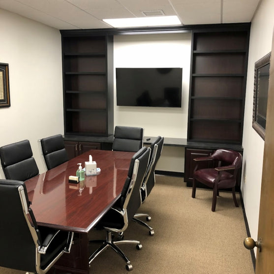 Conference room with a large wooden table, chairs, and a TV on the wall.
