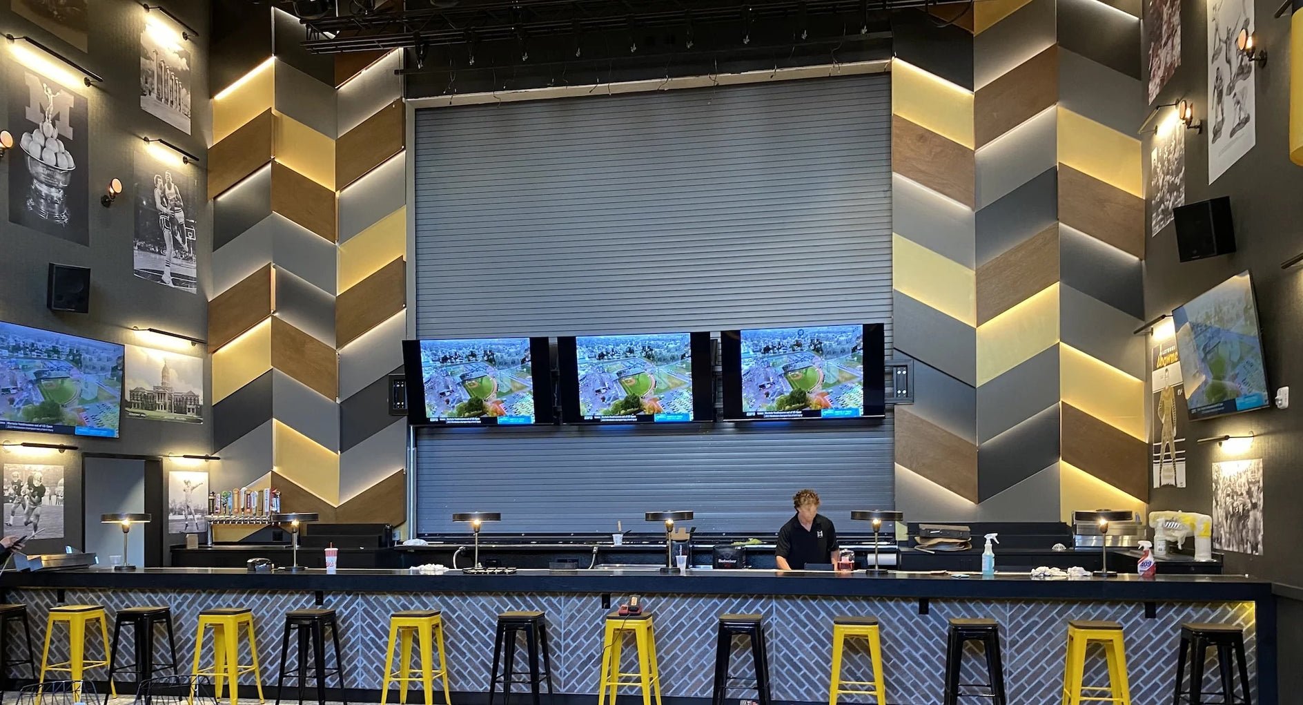 Modern bar with black and yellow stools, black bar counter, and multiple televisions on the wall.