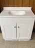 The Vanity with top features a white cabinet with a cultured marble top, built-in sink, and two doors for bathroom storage, shown against a wood-paneled wall on a tiled floor.
