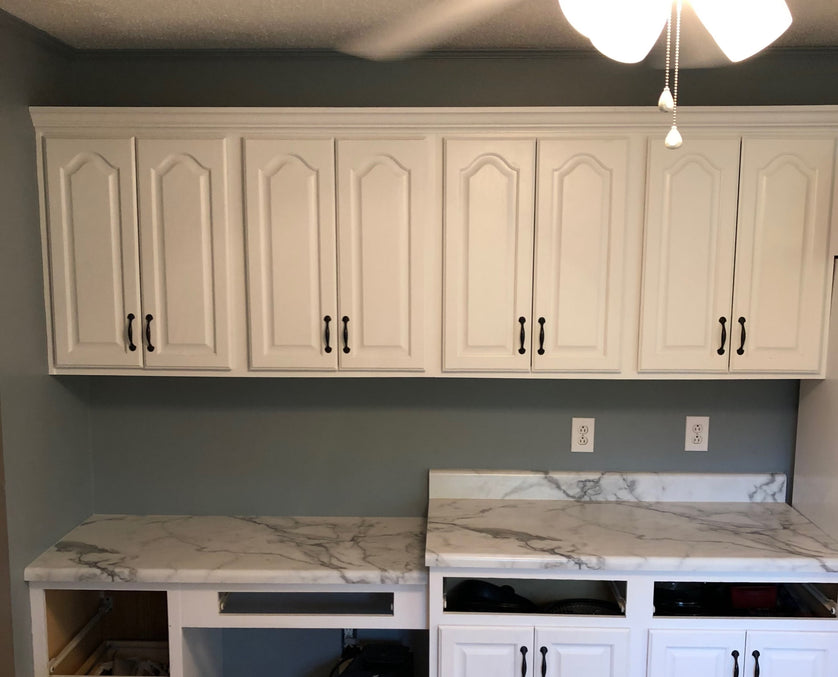 Kitchen with white cabinets and marble countertops against a gray wall.